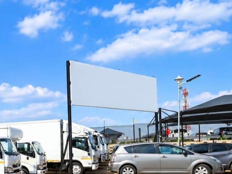 Commercial parking area featuring a large billboard structure and covered parking bays with shade cloth.