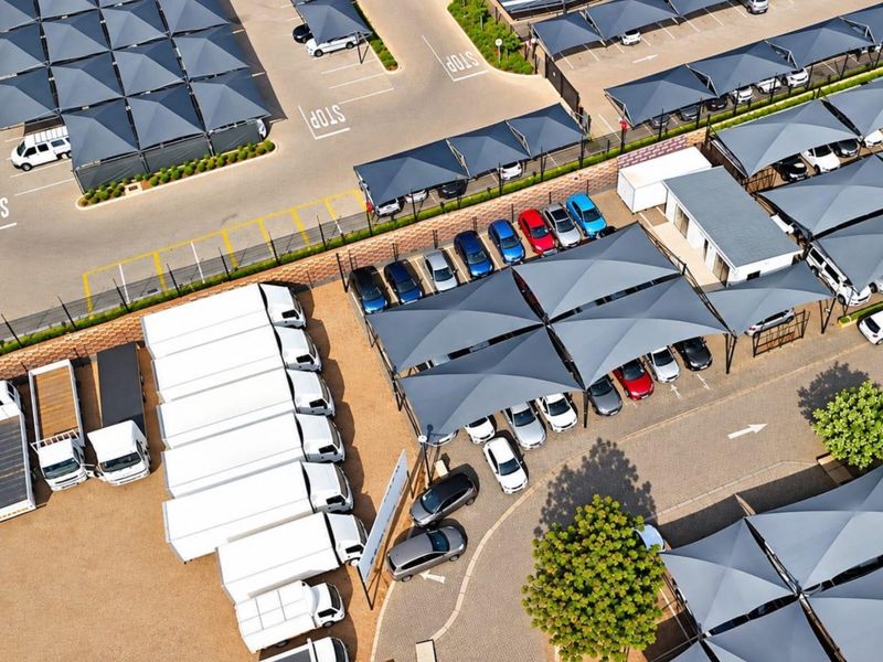 Aerial view of a commercial parking facility featuring extensive shade cloth carports, paved parking bays, and secure perimeter fencing.