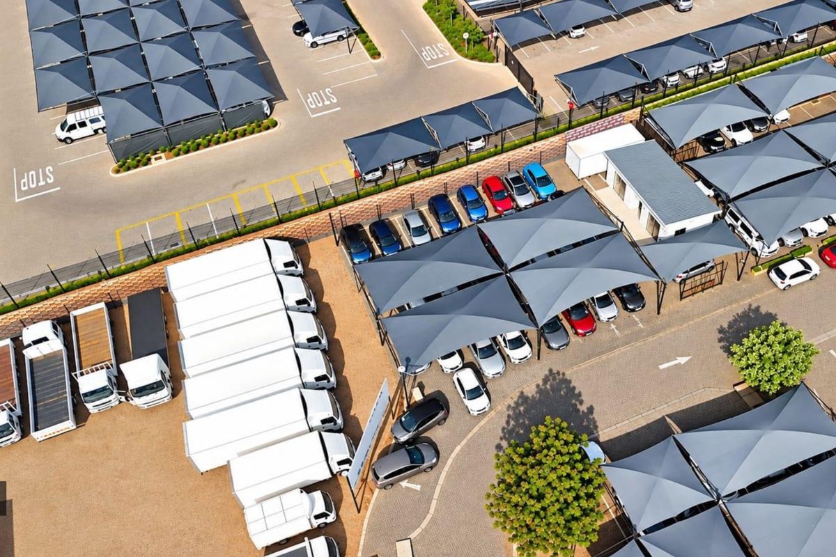 Aerial view of a commercial parking facility featuring extensive shade cloth carports, paved parking bays, and secure perimeter fencing.