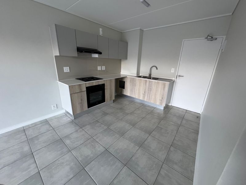 Modern kitchen featuring light wood-finish cabinetry, stone countertops, built-in oven and hob, and neutral tiled flooring in an open-plan layout.