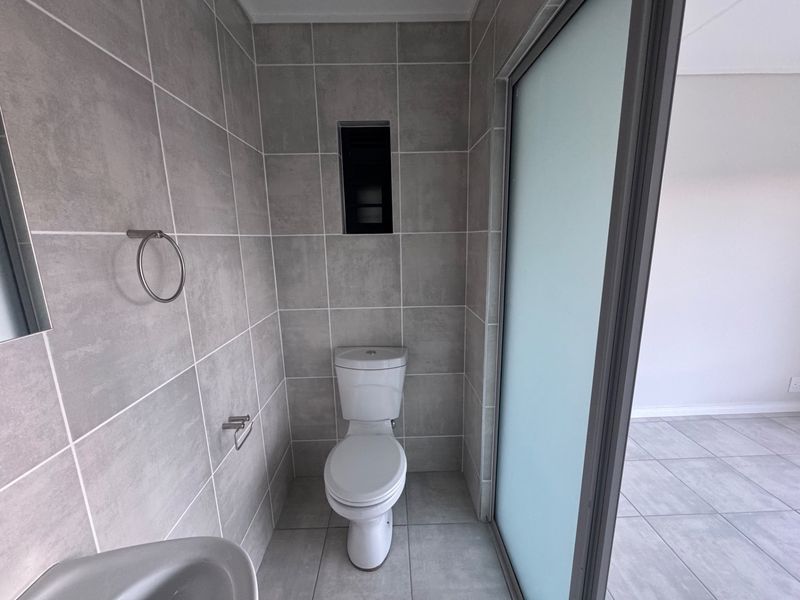 A modern, neutral-toned bathroom featuring floor-to-ceiling grey tiling, a standard toilet, and a frosted glass sliding door.