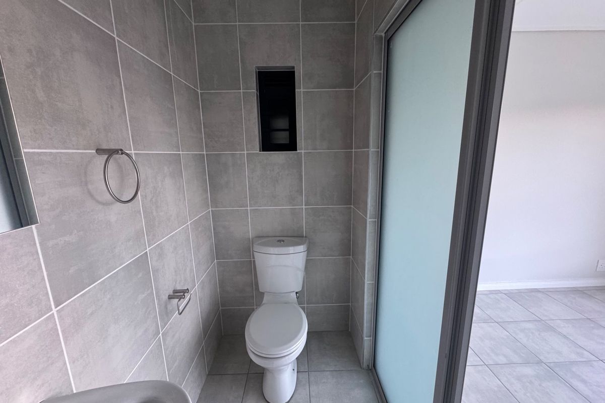 A modern, neutral-toned bathroom featuring floor-to-ceiling grey tiling, a standard toilet, and a frosted glass sliding door.