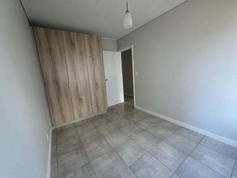 A clean, empty bedroom featuring modern grey floor tiles and built-in wood-finish cupboards, offering a neutral canvas for personalization.