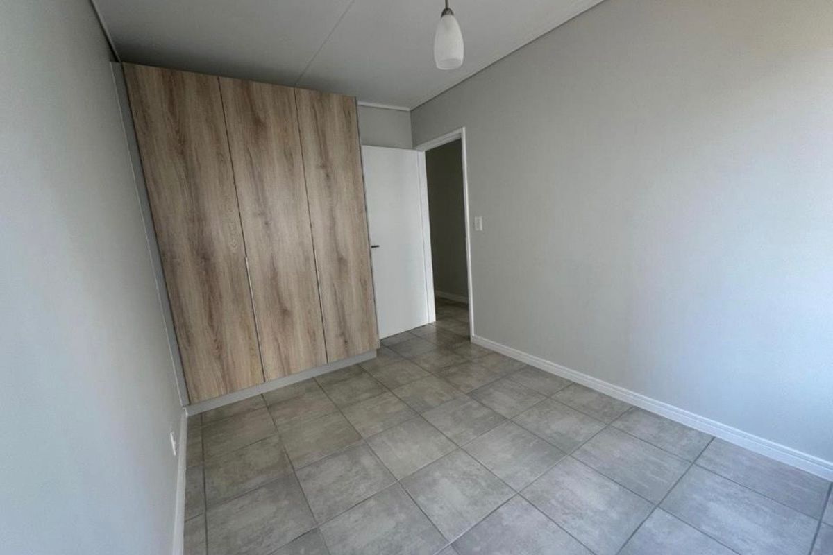 A clean, empty bedroom featuring modern grey floor tiles and built-in wood-finish cupboards, offering a neutral canvas for personalization.