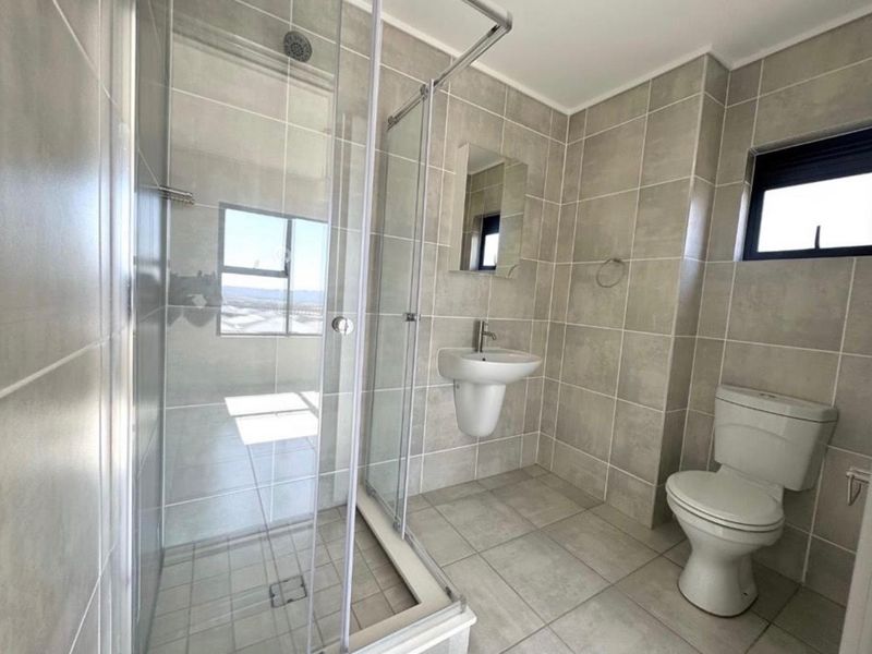 A clean, modern bathroom featuring a glass shower enclosure, wall-mounted basin, and neutral floor-to-ceiling tiling.