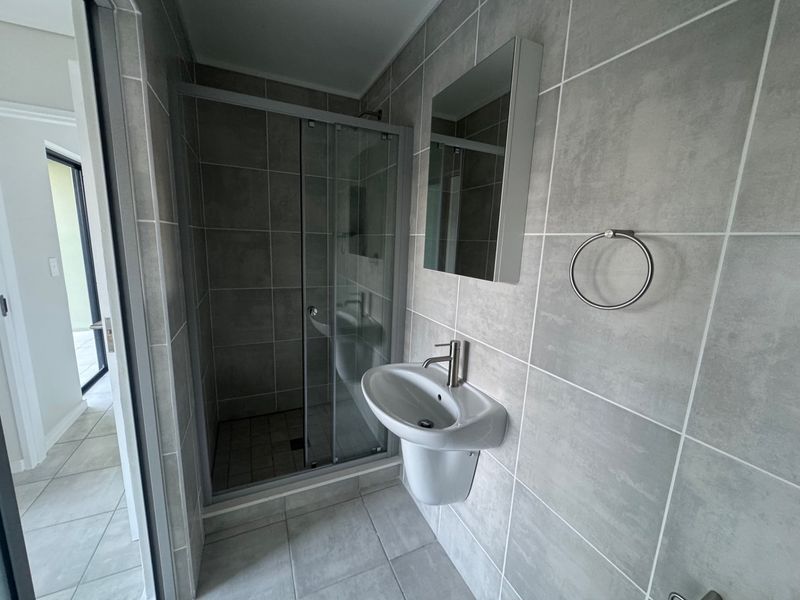 Modern bathroom featuring a glass shower enclosure, pedestal basin with mixer tap, and neutral grey wall and floor tiling.