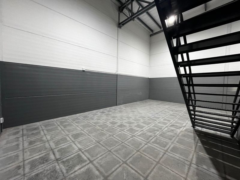 Spacious industrial utility area featuring high ceilings with exposed steel trusses, durable tiled flooring, and a modern metal staircase.