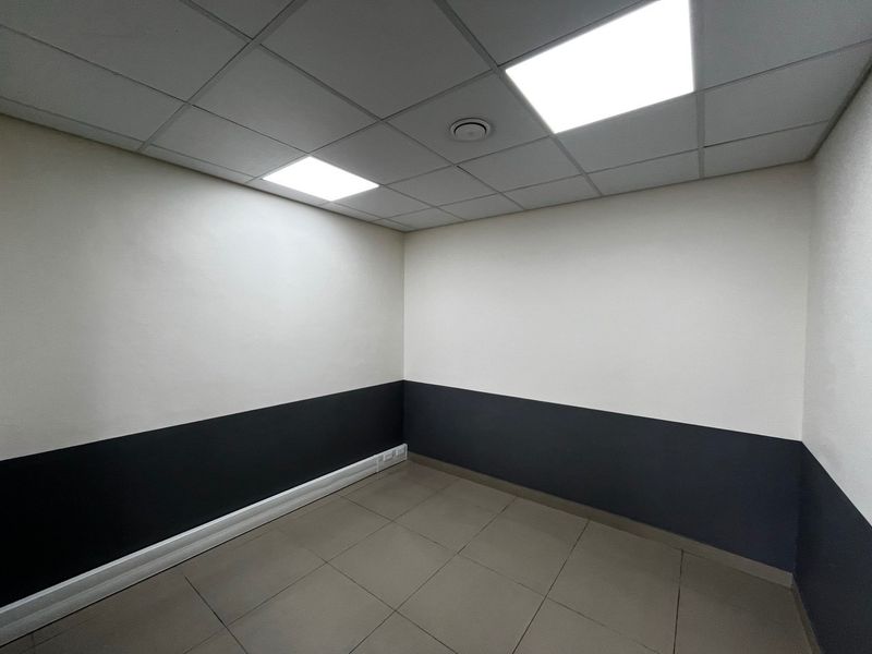 A clean, empty office space featuring a suspended ceiling with recessed LED lighting, tiled flooring, and two-tone wall finishes.