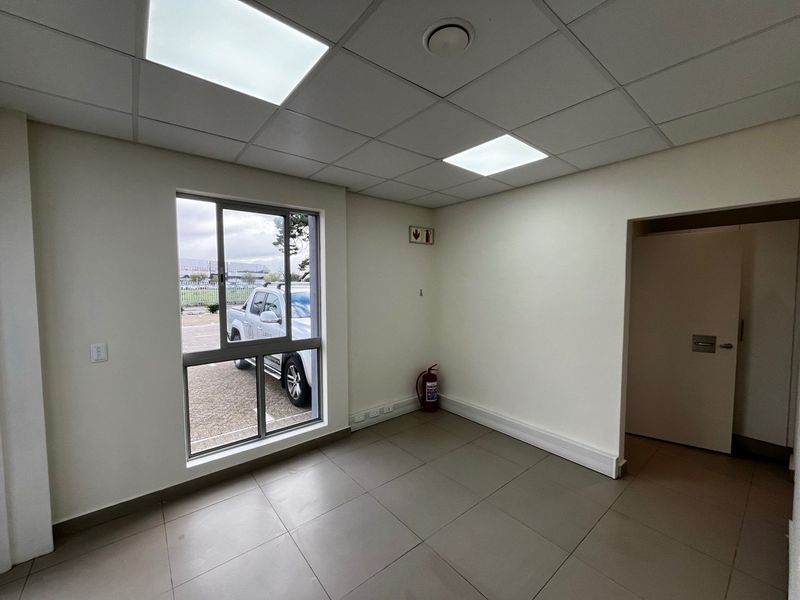 A clean, vacant office space featuring tiled flooring, a suspended ceiling with recessed lighting, and a large window providing natural light.