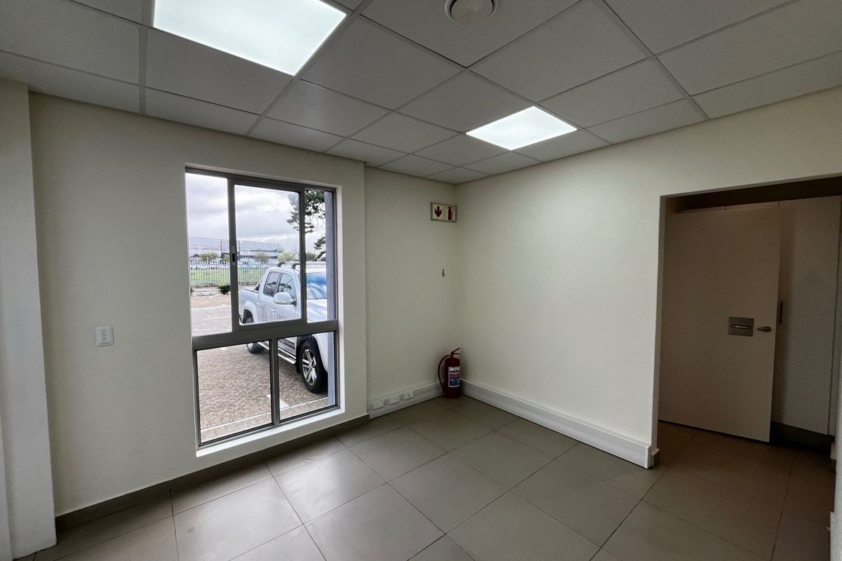 A clean, vacant office space featuring tiled flooring, a suspended ceiling with recessed lighting, and a large window providing natural light.