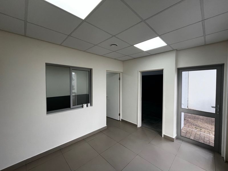 A clean, modern office space featuring tiled flooring, a suspended ceiling with recessed lighting, and aluminium-framed windows and doors.