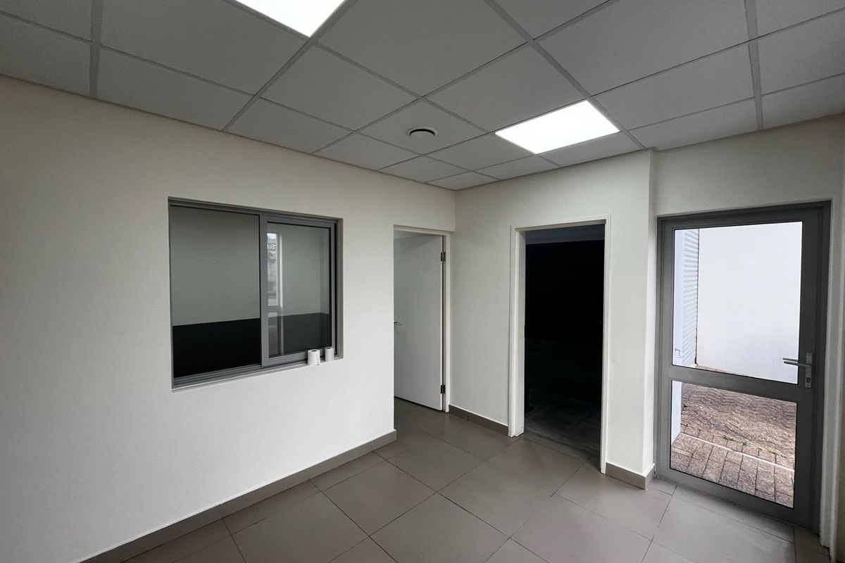 A clean, modern office space featuring tiled flooring, a suspended ceiling with recessed lighting, and aluminium-framed windows and doors.