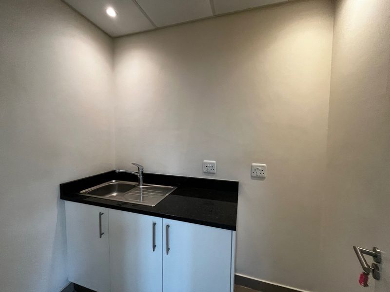 A compact utility or scullery area featuring a stainless steel sink, black granite countertop, and white base cabinetry with integrated electrical points.