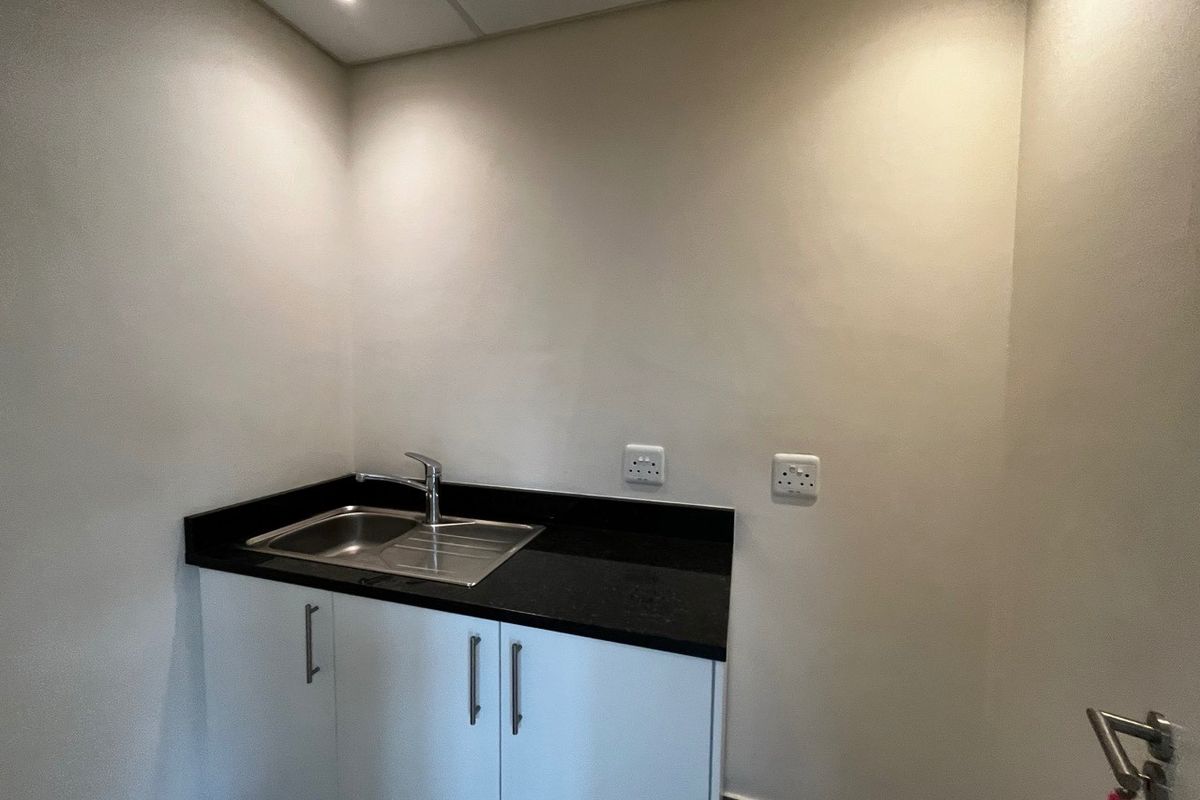 A compact utility or scullery area featuring a stainless steel sink, black granite countertop, and white base cabinetry with integrated electrical points.