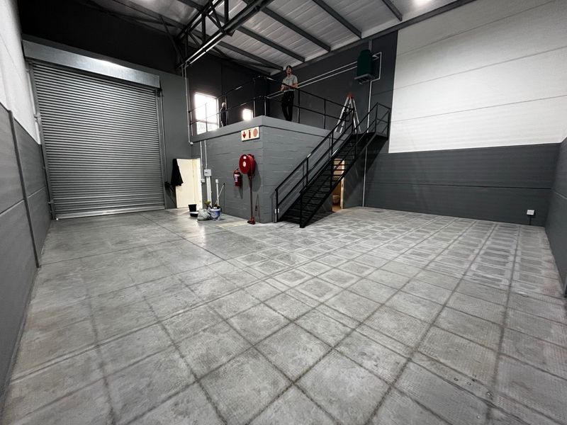 Spacious industrial warehouse unit featuring a high-clearance roller shutter door, mezzanine level with staircase access, and durable concrete flooring.