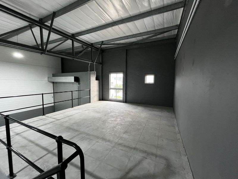 An open-plan industrial mezzanine level featuring exposed steel roof trusses, concrete flooring, and metal safety railings, suitable for storage or office conversion.