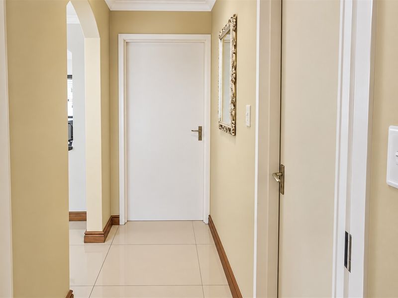 A clean and well-maintained hallway featuring neutral wall tones, tiled flooring, and an arched transition to adjacent living spaces.