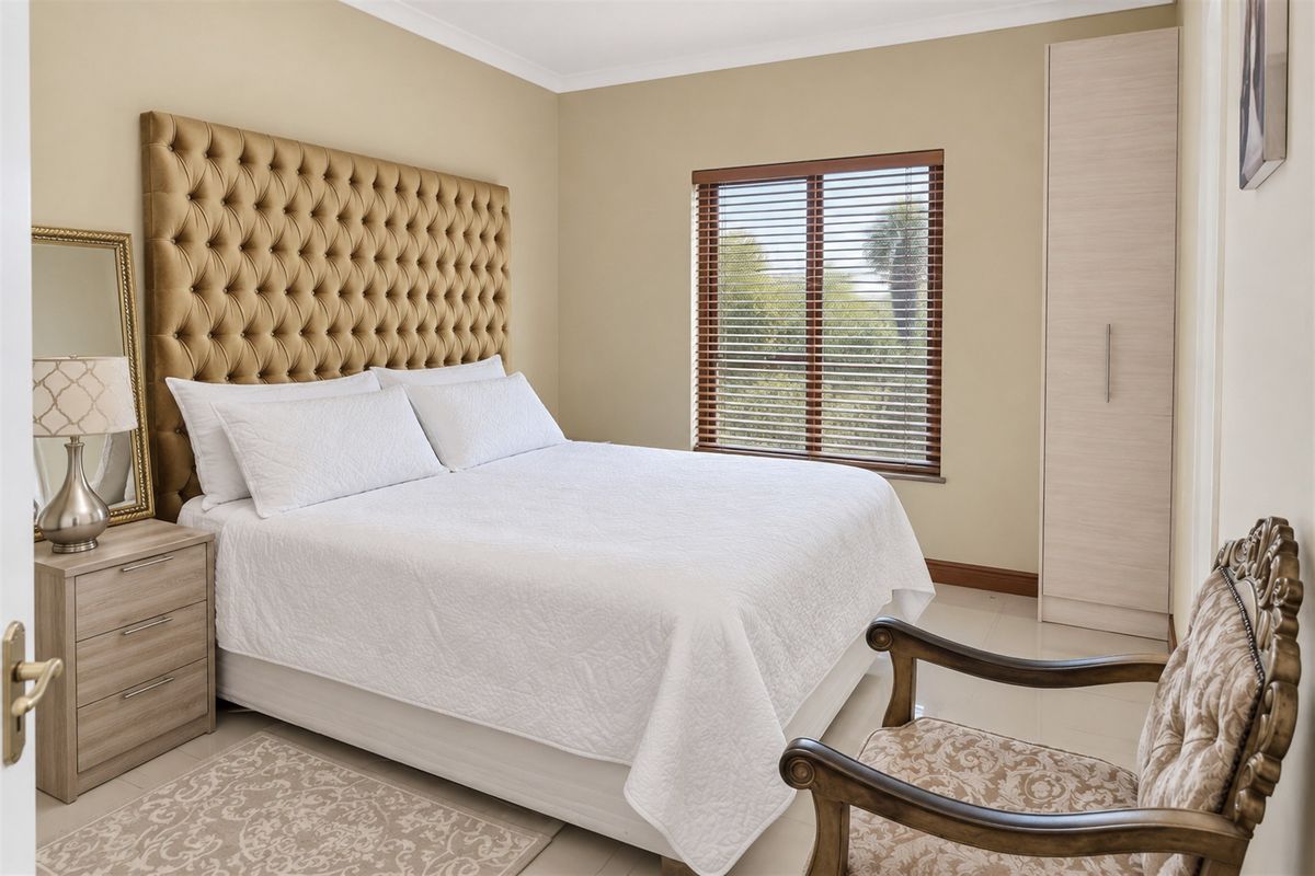 A well-maintained bedroom featuring neutral wall tones, tiled flooring, a built-in wardrobe, and venetian blinds allowing natural light.