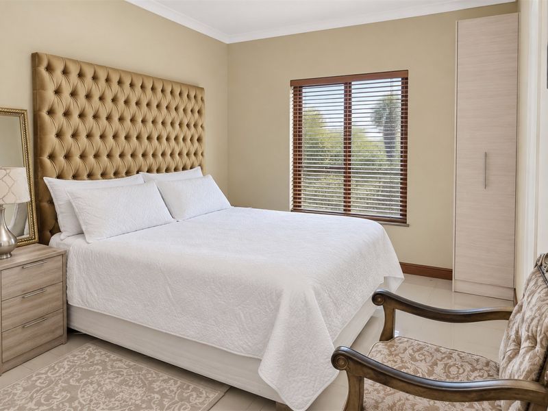 A well-maintained bedroom featuring neutral wall tones, tiled flooring, a built-in wardrobe, and venetian blinds allowing natural light.
