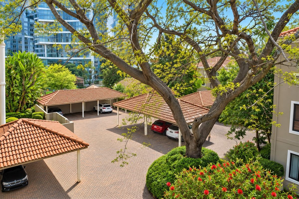 An elevated view of a well-maintained residential complex featuring multiple covered carports with terracotta tiled roofs and a paved driveway area.
