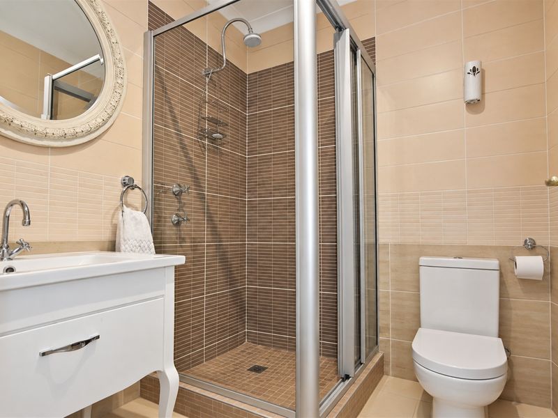 A well-maintained bathroom featuring a glass-enclosed shower, a modern vanity basin, and neutral-toned wall and floor tiling.
