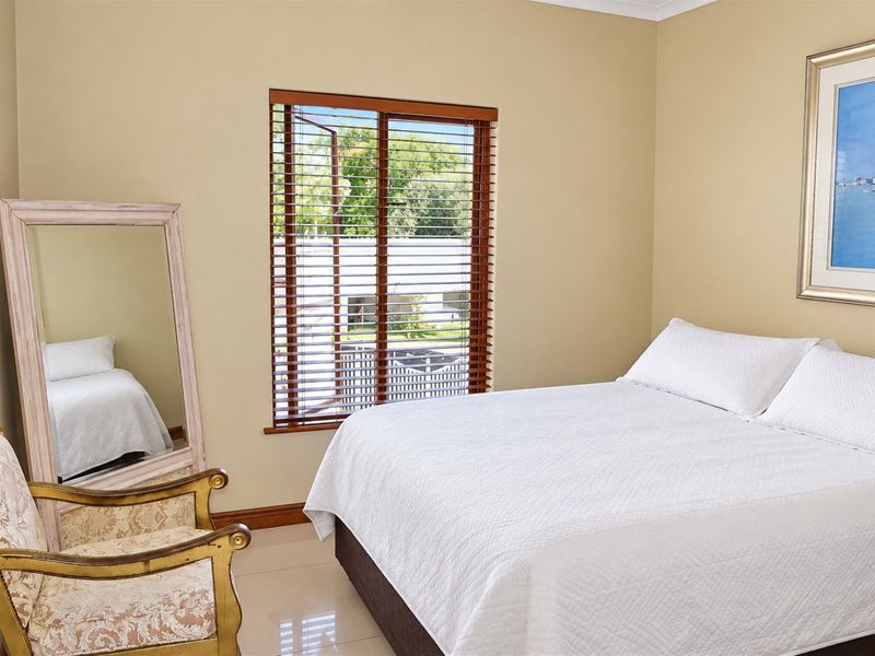 A well-maintained bedroom featuring neutral wall tones, tiled flooring, and wooden venetian blinds, offering a clean and comfortable living space.