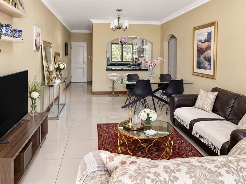 Spacious open-plan living and dining area featuring polished porcelain tiles, elegant crown molding, and a convenient kitchen pass-through archway.