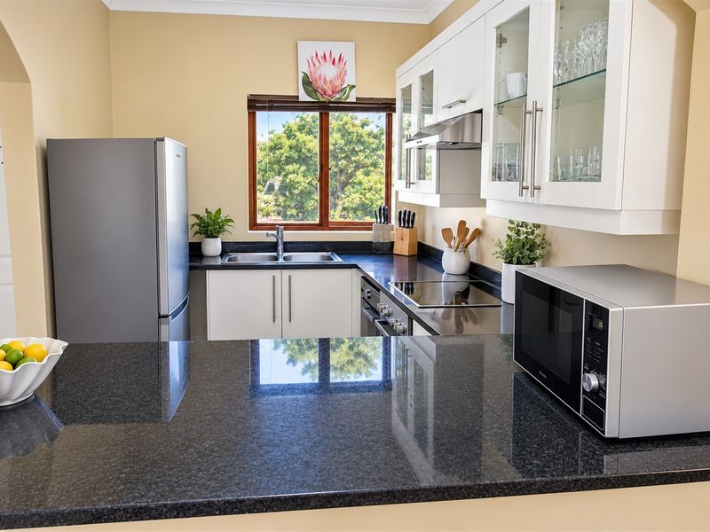 A well-maintained kitchen featuring dark granite countertops, white cabinetry with glass-fronted display units, and integrated stainless steel appliances.