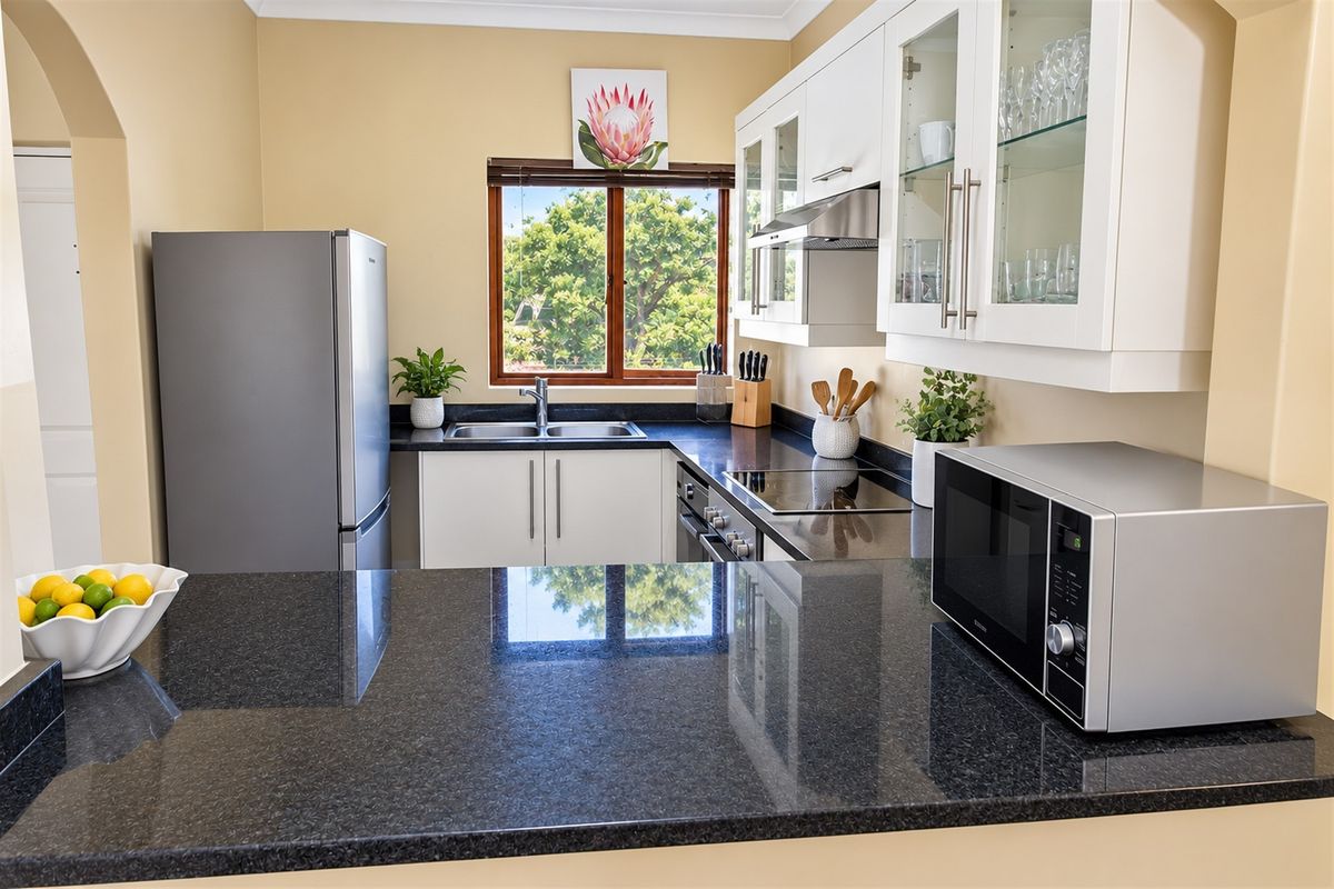 A well-maintained kitchen featuring dark granite countertops, white cabinetry with glass-fronted display units, and integrated stainless steel appliances.