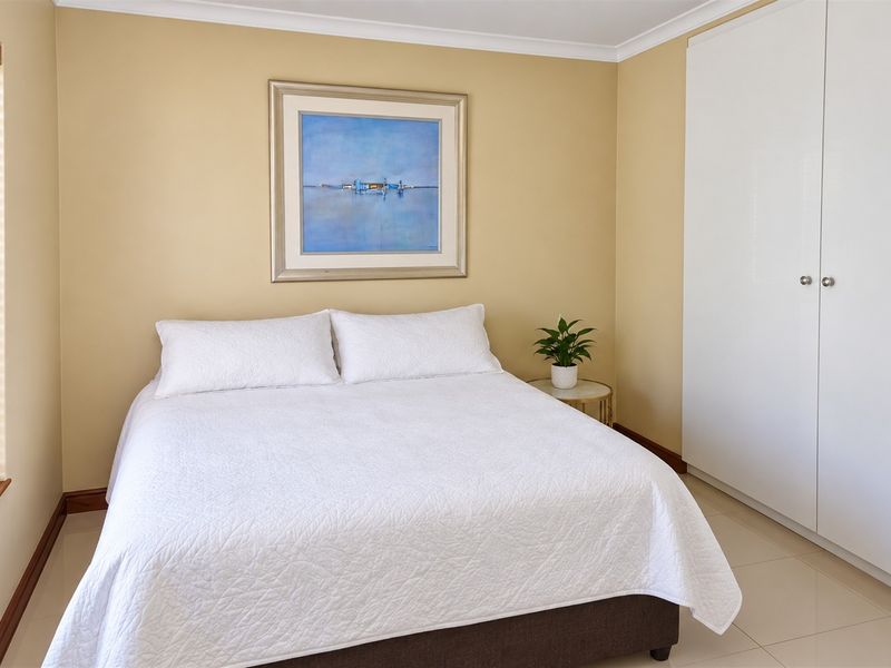A well-maintained bedroom featuring neutral walls, tiled flooring, and a large built-in wardrobe with clean white finishes.