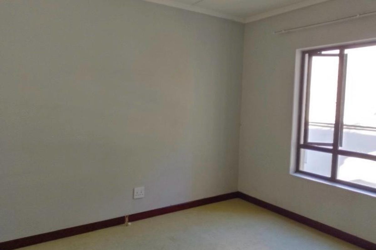 An empty bedroom featuring neutral walls, carpeted flooring, and a window with a curtain rail.