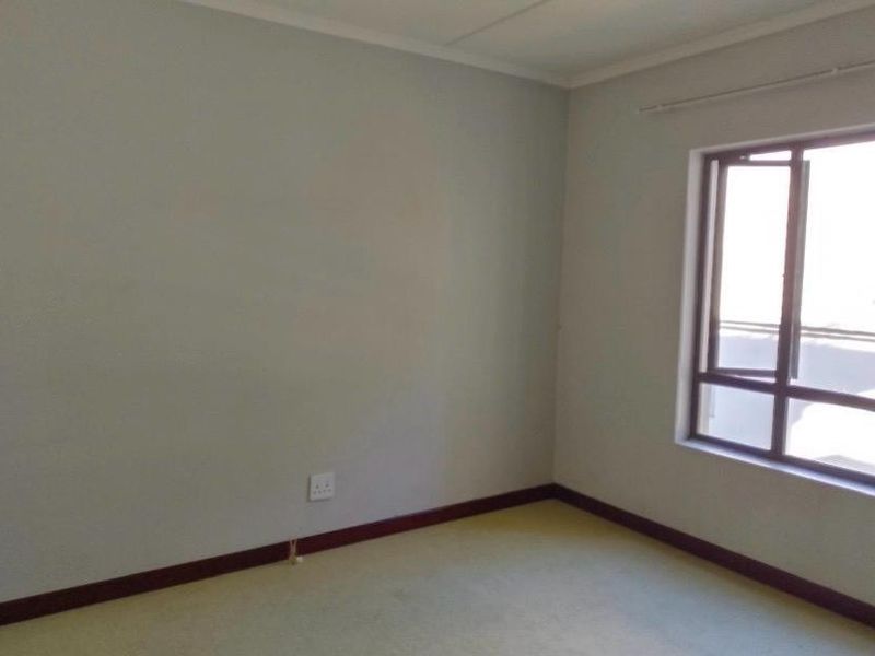 An empty bedroom featuring neutral walls, carpeted flooring, and a window with a curtain rail.