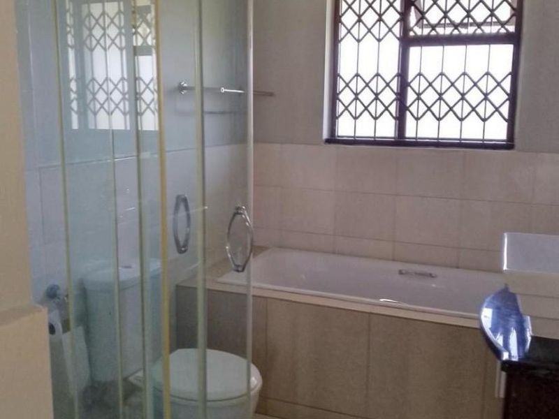 A functional bathroom featuring a glass shower enclosure, a built-in bathtub, tiled surfaces, and a vanity basin with security bars on the window.