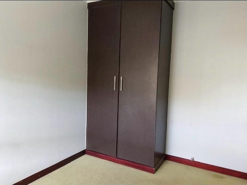 A simple bedroom featuring a dark brown built-in wardrobe and neutral carpeting.