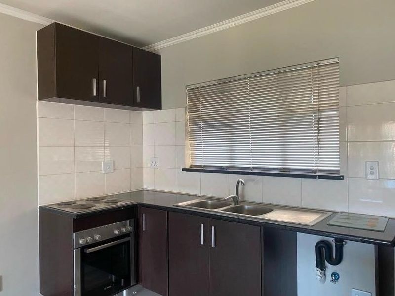 A functional kitchen featuring dark wood cabinetry, a built-in electric oven and hob, tiled splashback, and a stainless steel double sink.
