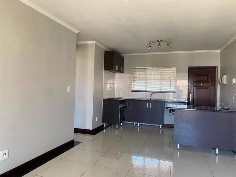 An open-plan living and kitchen area featuring tiled flooring, dark cabinetry, and a functional kitchen layout with a breakfast counter.