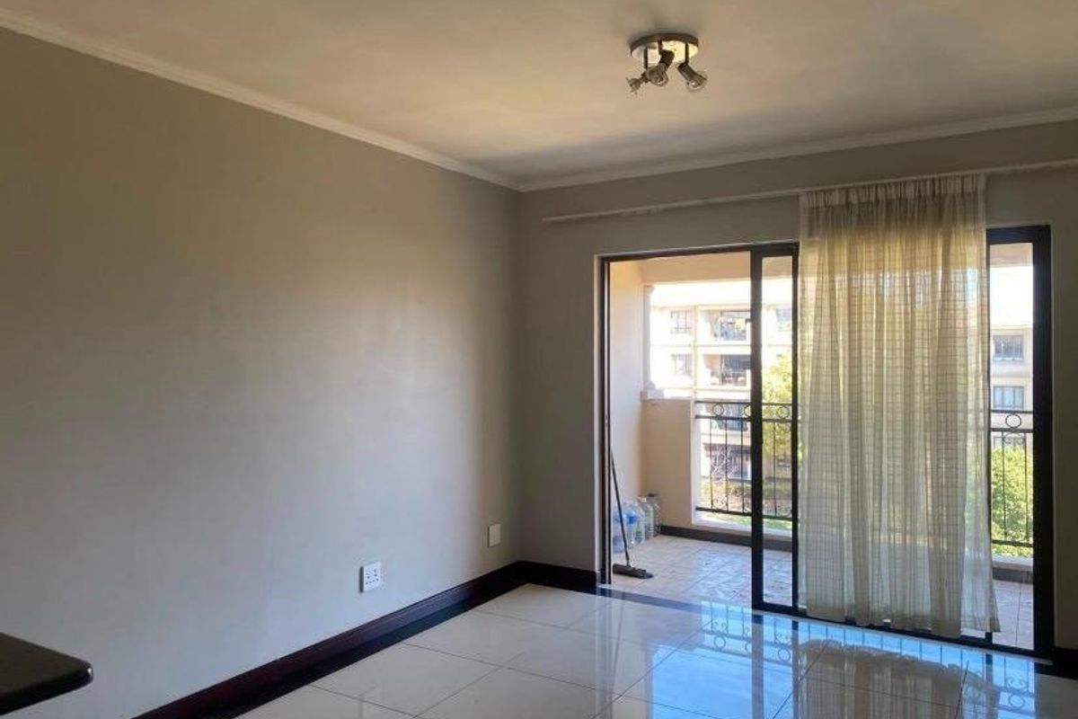 A bright, empty living area featuring neutral walls, tiled flooring, and a sliding glass door providing access to an outdoor balcony.