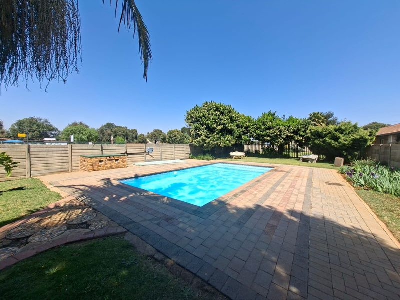 A well-maintained outdoor pool area featuring a paved deck, a built-in brick braai, and secure perimeter walling in a private garden setting.