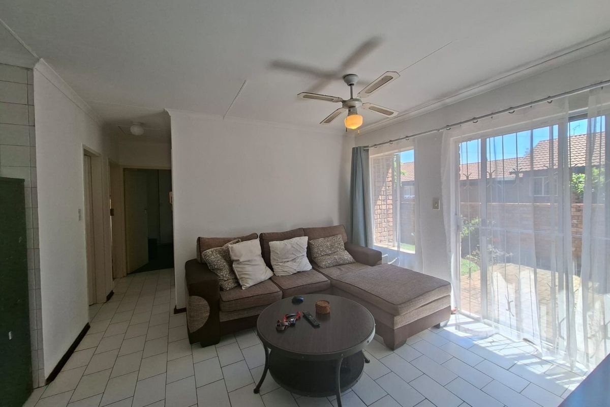 A bright living room featuring tiled flooring, a ceiling fan, and large sliding glass doors providing direct access to the rear garden area.