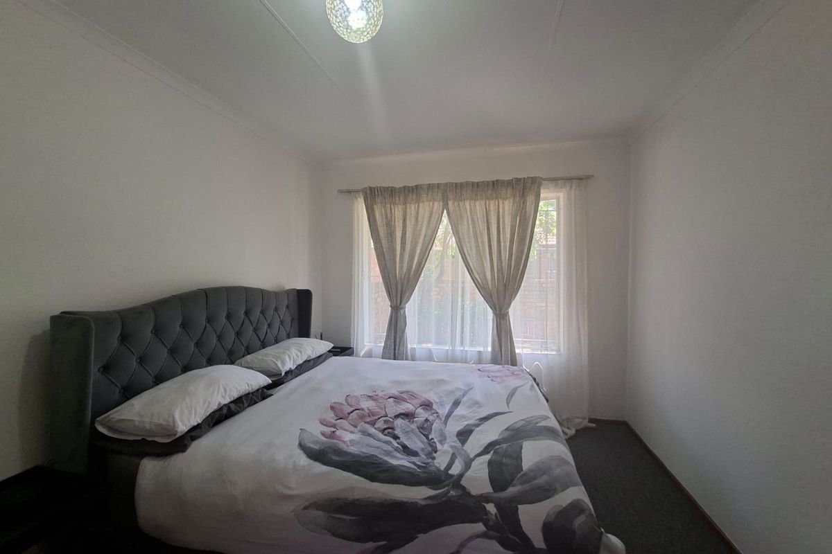A standard bedroom featuring neutral walls, carpeted flooring, and a window with installed curtain rods.