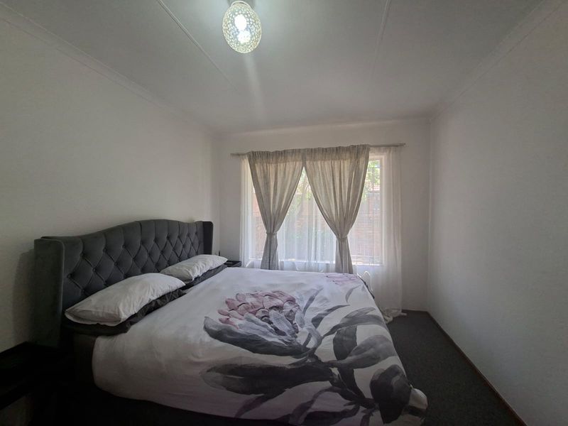 A standard bedroom featuring neutral walls, carpeted flooring, and a window with installed curtain rods.