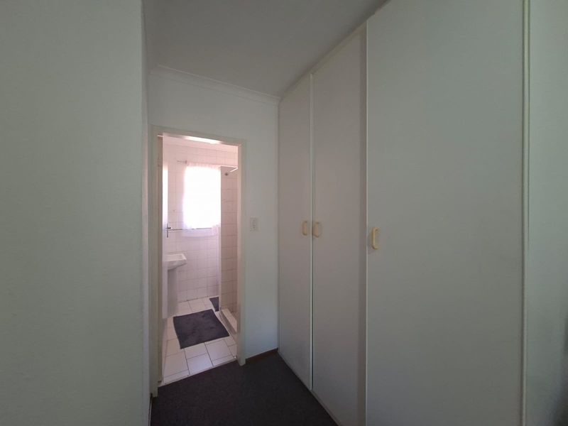A hallway featuring built-in cupboards with direct access to an adjacent bathroom equipped with a pedestal basin and shower.