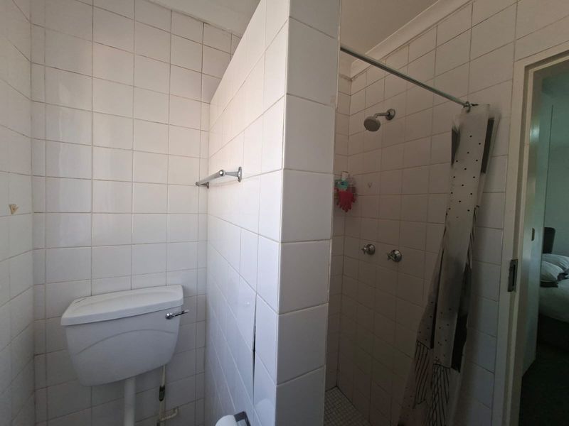 A functional bathroom featuring a tiled shower enclosure and a standard toilet, showing signs of wear and requiring cosmetic updates.