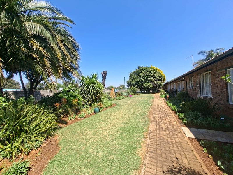 A well-maintained rear garden area featuring a brick-paved walkway, established landscaping, and a brick townhouse exterior with security bars on the windows.