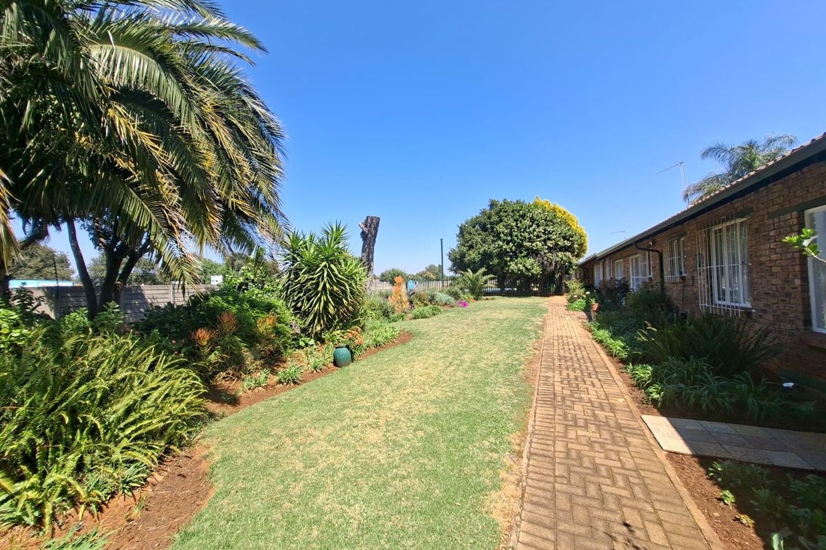 A well-maintained rear garden area featuring a brick-paved walkway, established landscaping, and a brick townhouse exterior with security bars on the windows.