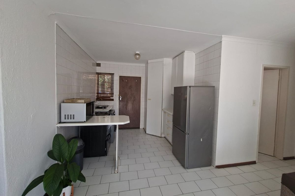 A functional kitchen featuring tiled flooring, white tiled splashbacks, built-in cabinetry, and a breakfast counter, offering a clean but dated aesthetic.