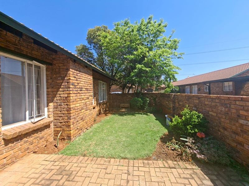 A private rear garden area featuring a paved patio, a small lawn, and face brick boundary walls, providing a low-maintenance outdoor space.