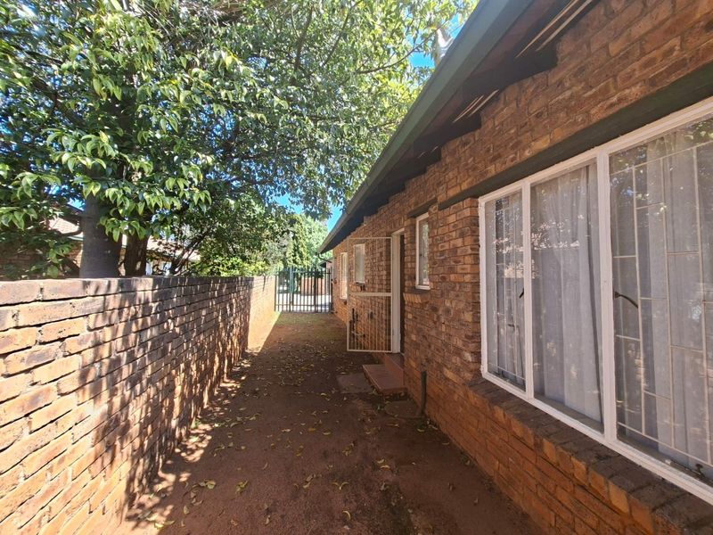 A side exterior view of the townhouse featuring face brick walls, security gates, and security bars on the windows.