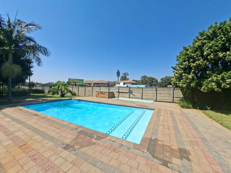 Outdoor pool area featuring a paved deck, swimming pool, and a built-in brick braai, enclosed by a perimeter boundary wall.