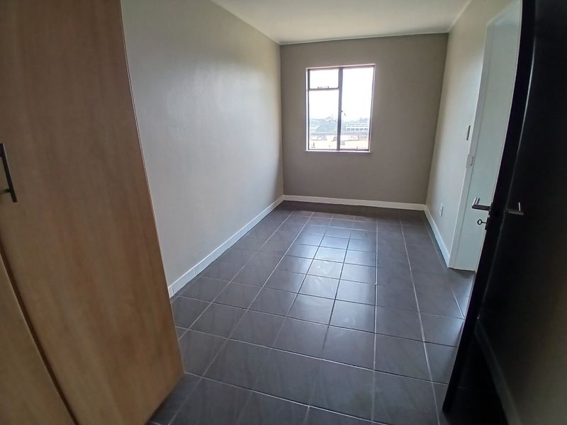 A clean, empty bedroom featuring neutral wall tones, tiled flooring, and a built-in cupboard, offering a versatile space ready for personalization.